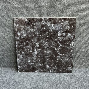 Foto einer einzelnen quadratischen Bodenfliese in schwarzer Farbe, stark marmoriert, mit Naturkante.