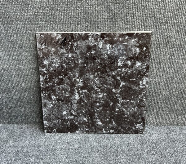 Foto einer einzelnen quadratischen Bodenfliese in schwarzer Farbe, stark marmoriert, mit Naturkante.
