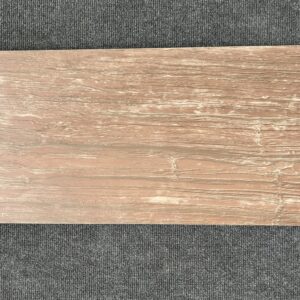 Foto einer einzelnen Bodenfliese Feinsteinzeug im Format 30 cm x 60 cm. Diese Fliese hat einen rötlichen Braunton und ist in Holzoptik gehalten, die kaum von echtem Holz zu unterscheiden ist.